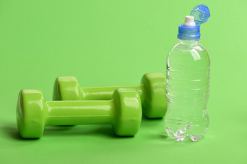 Water bottle near lightweight barbells, close up. Athletics concept