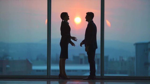 The man and a woman talking near the panoramic window on a sunset background