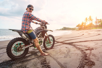 Biker man with his sport motorbike on black sand beach.