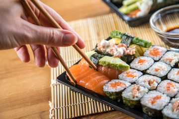 Frau isst Lachs Sushi Nigiri mit Stäbchen aus Bento Box mit Sojasoße