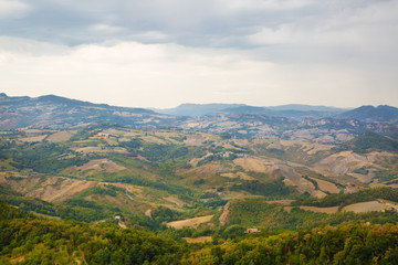 Fototapeta na wymiar Panoramic view of San Marino. Green valley with orange roofs houses. Cloudly sky in summer.