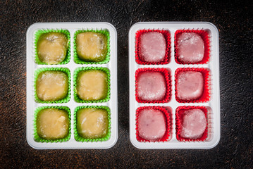 Two kinds of mochi, green and pink, dark rusty background. Copy space top view
