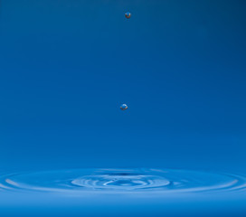 drop of water liquid with splash isolated. the drop explodes in the water sending spray to the sides and circle ripples around it. the water is blue