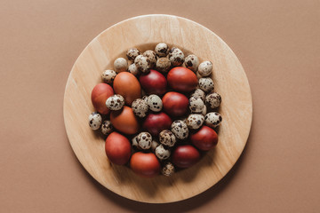 top view of chicken and quail easter eggs on wooden plate
