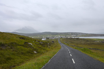 Nature road on the coast of Ireland with the mountains on the background after rain with gray clouds