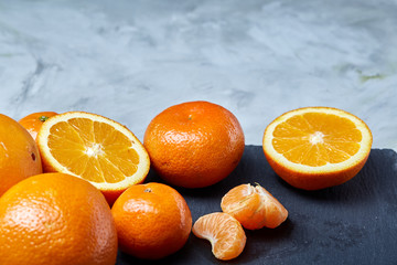 Pile of whole and half cut fresh tangerine and orange on cutting board, close-up