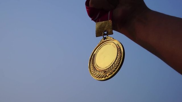 Winners Champion in success award concept : Woman hands raised holding gold medals with ribbon against blue sky background to show success in sport or business, Slow motion