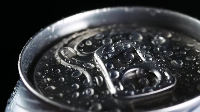 A cold drink rotates against a black background. Water droplets on aluminium can of soda or beer
