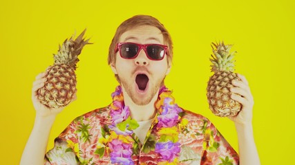 Happy lucky young man standing on yellow background with hawaiian shirt and two pineapples