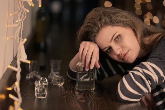 Young woman with bottle of drink in bar. Alcoholism problem