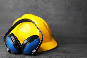 Headphones and hard hat on table against grey background. Hearing protection equipment
