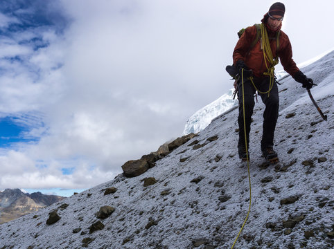 male mountain climber descending a steep snow and scree slope in the Cordillera Blanca in Peru on his way to base camp after submitting a high peak