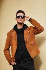 Model looking man stand near the wall and hold his glasses towards the sun shine