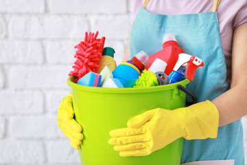 Woman holding bucket with cleaning supplies on brick wall background © Africa Studio