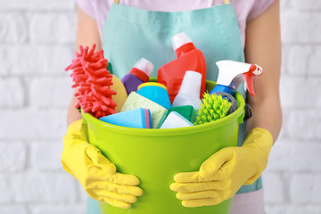 Woman holding bucket with cleaning supplies on brick wall background