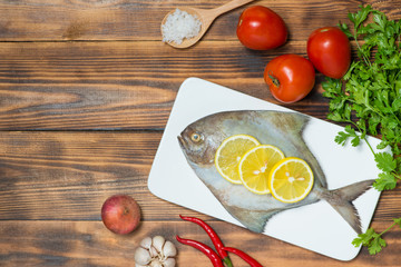 Fish dish cooking with various ingredients. Fresh raw fish decorated with lemon slices and herbs on wooden table.