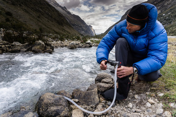 man in blue down jacket filtering water from a river for drinking and cooking in a high mountain valley in the Andes of Peru