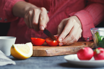 Girl in a pink shirt slices a fresh tomato on a textured wooden board surrounded by vegetables. A series of photos about the preparation of summer vegetable salad.