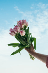 A vertical image of bouquet of pink flowers in a hand against blue sky background