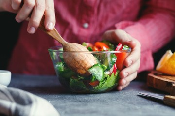 Girl in a pink shirt is moving a wooden spoon with a salad of fresh vegetables. A series of photos...