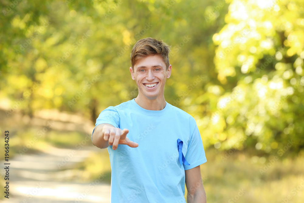 Wall mural Young man in t-shirt with blue ribbon outdoors. Prostate cancer awareness concept