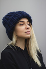 a blonde girl with big eyes and plump lips against a light gray background. woman in a voluminous warm dark blue cap