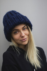 a blonde girl with big eyes and plump lips against a light gray background. woman in a voluminous warm dark blue cap