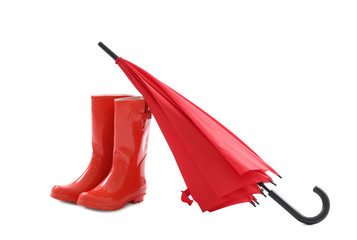 Stylish red umbrella and rubber boots on white background