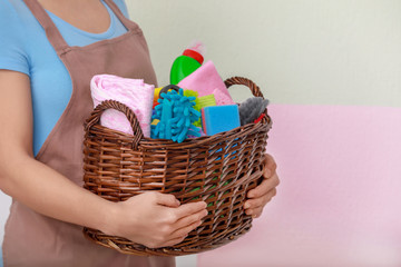 Fototapeta na wymiar Woman holding basket with cleaning supplies on color background