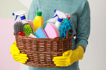 Woman holding basket with cleaning supplies on color background