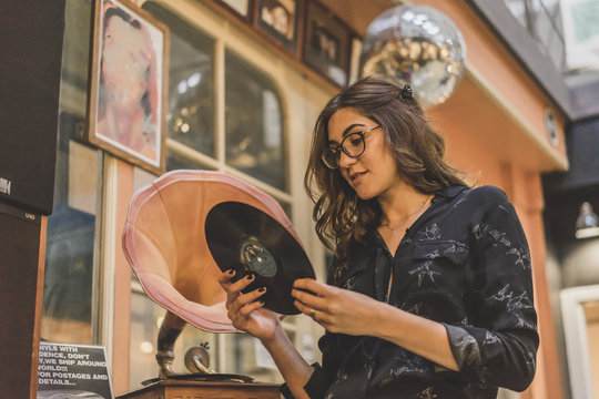 Portrait of smiling young woman standing in front of antique shop looking at gramophone record