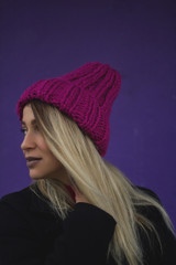 a blonde girl with big eyes and plump lips against a violet background. woman in voluminous warm color fuchsia hat.