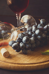 Two wineglasses with red wine and grapes decorated vine leaves on dark wooden desk. Toned