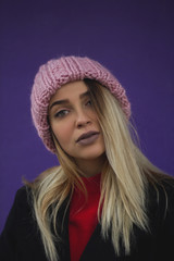 blonde girl with big eyes and plump lips against a violet background. woman in voluminous warm-colored powder hat.