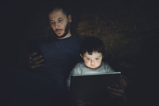 Father and daughter using phablet and digital tablet at home in the dark