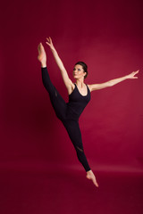 Obraz premium Beautiful slim flexible woman is wearing black body costume in studio isolated on red