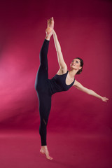 Obraz premium Beautiful slim flexible woman is wearing black body costume in studio isolated on red