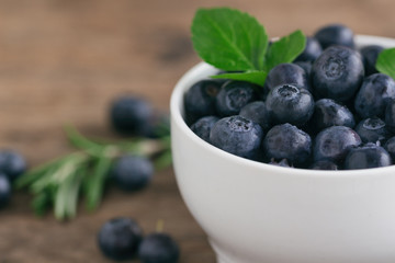 Fresh blueberries heap in white bowl in close up view macro concept with copy space on wood table for background. Blueberry is healthy and delicious fruits which have high antioxidant and vitamin C.