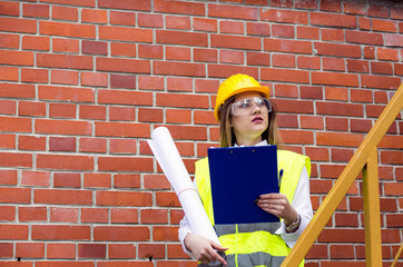 Industrial concept.Female engineer wearing safety vest and helmet using blueprint.