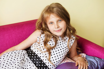 Naklejka premium portrait of a lovely little girl in polka dot dress resting on purple sofa