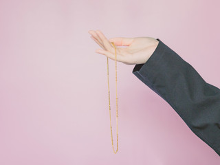 business and finance concept from beauty woman hand with black business suit hold gold necklace by right hand with pink pastel isolated background