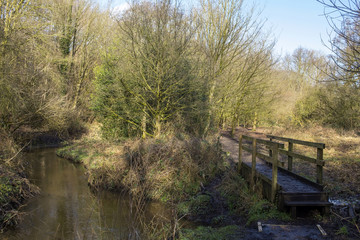 Fototapeta na wymiar Stream with public footpath over wooden bridge in Cheshire UK