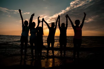 Zelfklevend Fotobehang group of six children raised their hands up silhouettes at sunset beach © kravtzov