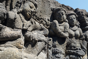 Fototapeta na wymiar Closeup wall ornamented with bas-reliefs depicting scene of life in ancient Java and people's faces. Highly detailed stone carving. Borobudur Buddhist temple, Magelang, Indonesia