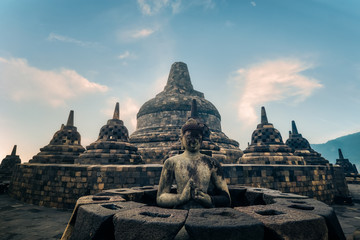 Fototapeta na wymiar Amazing statue of meditating Buddha and stone stupas against blue sky on background. Ancient Borobudur Buddhist temple. Great religious architecture. Magelang, Central Java, Indonesia