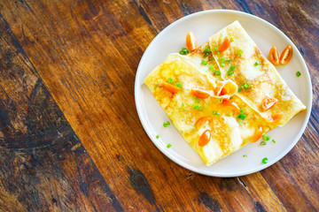 Pancakes (or crepes) with salmon and sauce. On a wooden table in the restaurant. The golden pancake crust is neatly wrapped in the filling: fish, mayonnaise, vegetables. Top view with copy space