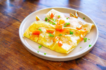Pancakes (or crepes) with salmon and sauce. On a wooden table in the restaurant. The golden pancake crust is neatly wrapped in the filling: fish, mayonnaise, vegetables. Top view with copy space