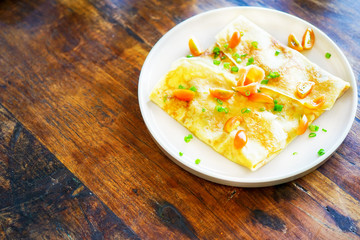 Pancakes (or crepes) with salmon and sauce. On a wooden table in the restaurant. The golden pancake crust is neatly wrapped in the filling: fish, mayonnaise, vegetables. Top view with copy space