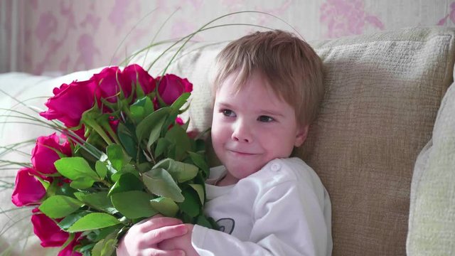 Happy baby holding a big bouquet of scarlet roses.A gift for mother's birthday