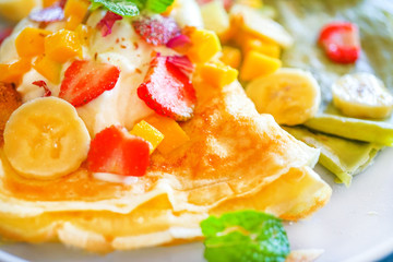 Pancakes (or crepes) with a matcha and ripe berries. On a wooden table in the restaurant. Golden pancake crust is neatly wrapped in a stuffing: bananas, strawberries, mint. Top view with copy space